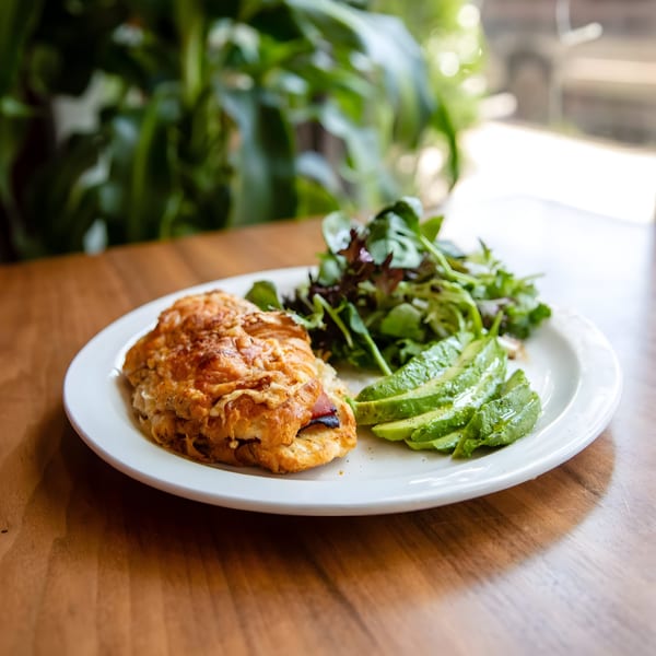 Zaca Cafe's savory croissant with a side of fresh greens and sliced avocado on a white plate.