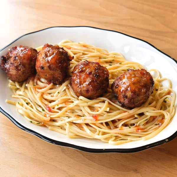 Zaca Cafe's spaghetti with four large, glazed meatballs in a white bowl on a wooden table.