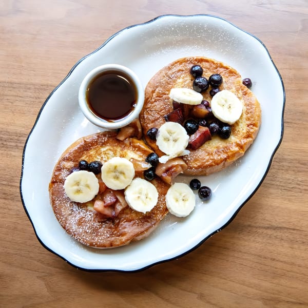 Two Zaca Cafe pancakes with blueberries, banana slices, and syrup on a white plate.