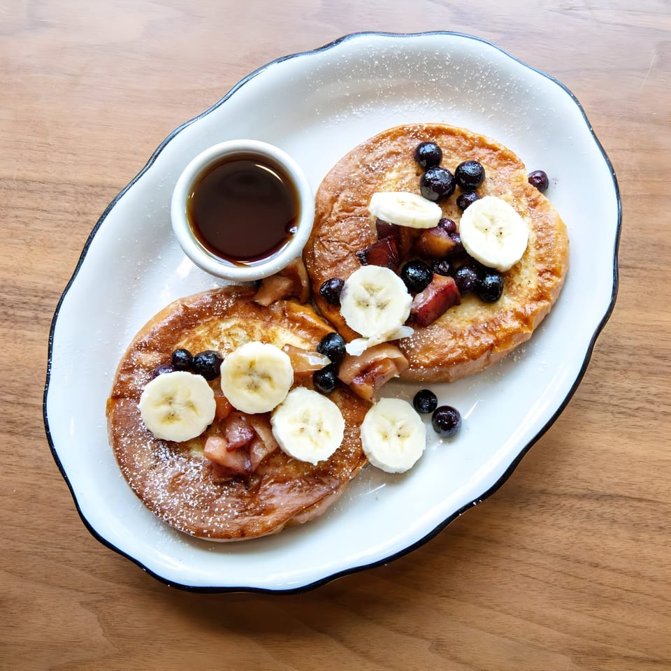 Two Zaca Cafe pancakes with blueberries, banana slices, and syrup on a white plate.