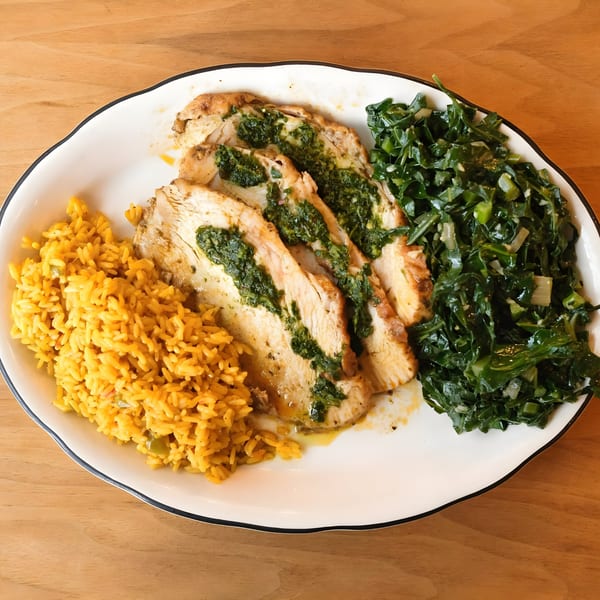 Zaca Cafe's sliced chicken with green sauce, yellow rice, and collard greens on a white plate.